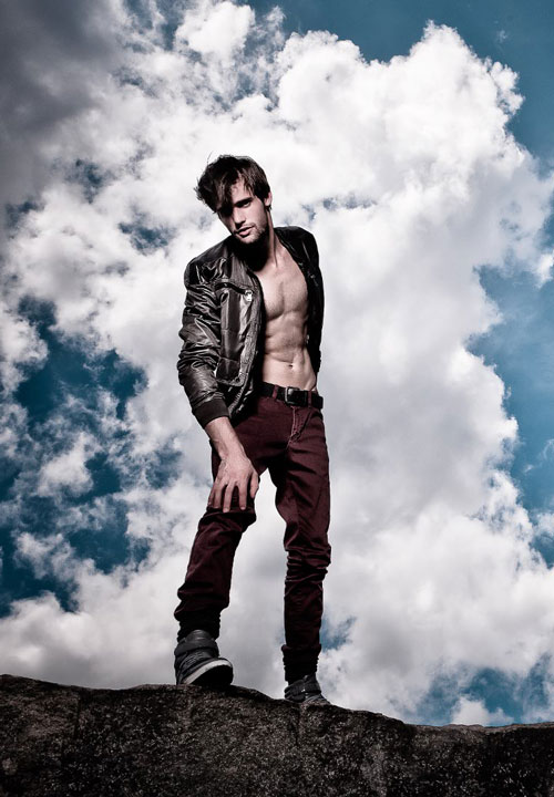 Alex Lago - model - Alex standing on a rock with a blue, cloudy sky behind him
