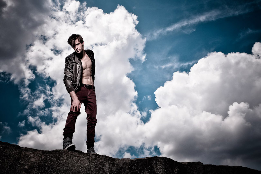 Alex Lago - model - Alex standing on a rock with the blue sky and clouds behind him